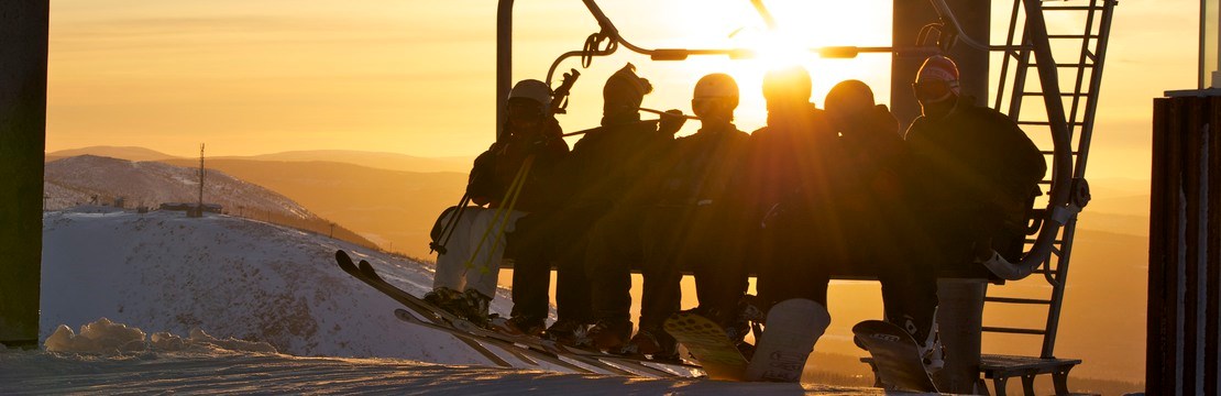 Ett gäng skidåkare i en sittlift med solnedgång i bakgrunden.