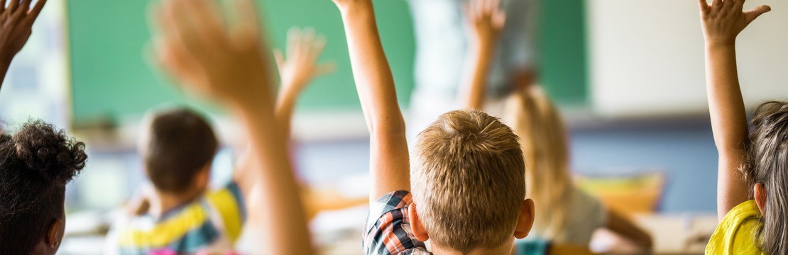 Barn i ett klassrum som räcker upp händerna.