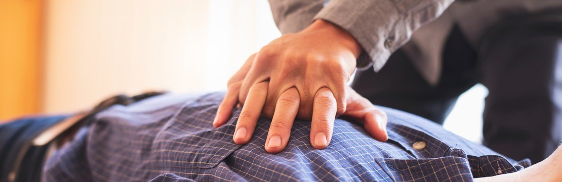 Händer utför akut hjärt-lungräddning på man med skjorta.