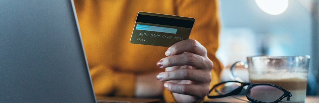 Kvinna framför dator med betalkort i handen.