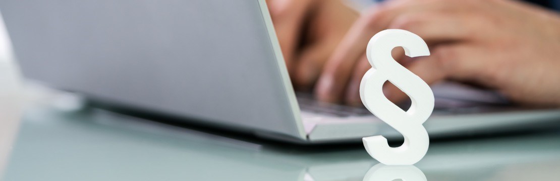 Ett vitt paragraftecken står intill en öppnad laptop, där en person sitter och skriver vid tangentbordet.