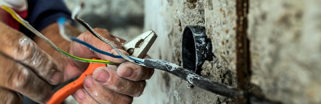 Hand på elinstallatör som skalar av isolering på kablar.