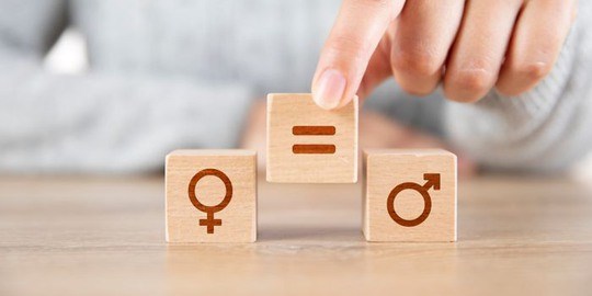 Kvinnlig hand som placerar en träkloss med symbolen "lika med" mellan två klossar, en av dem med ikonen för kvinna  och den andra med ikonen för man.