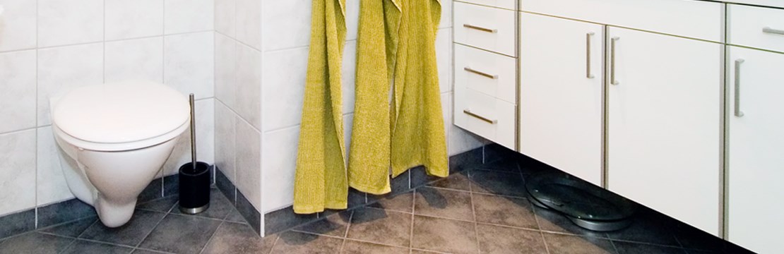 Bild från badrum med kaklade väggar och golv. Gula handdukar hänger på vägg.